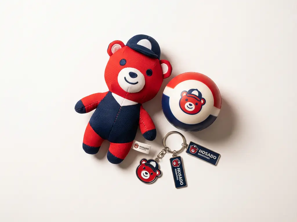 Custom branded promotional items including a plush mascot, stress ball, and keychain in matching red, white, and navy on a white surface.